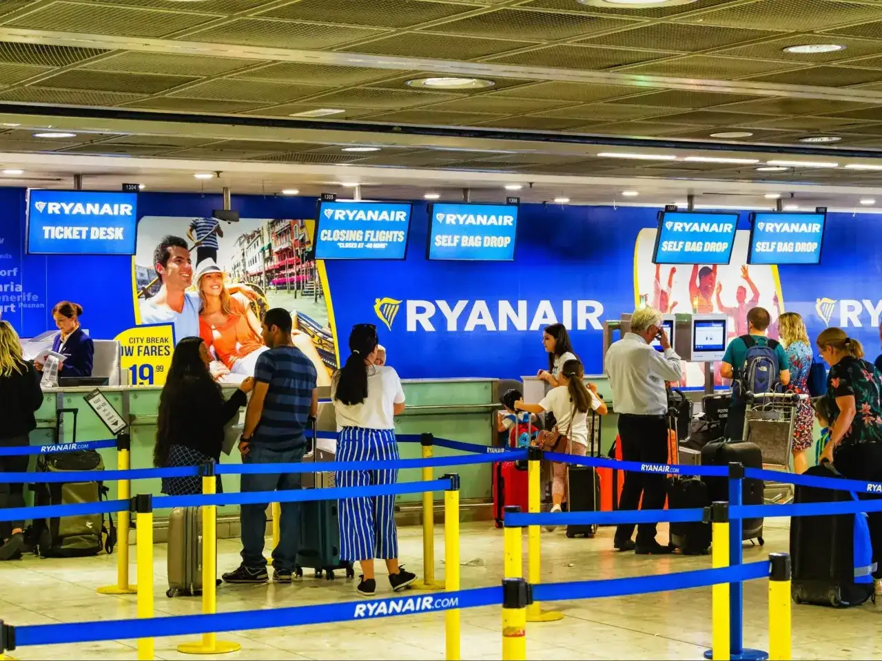 Kasa biletowa i punkty odprawy bagażu Ryanair na lotnisku, z ludźmi i bagażami.