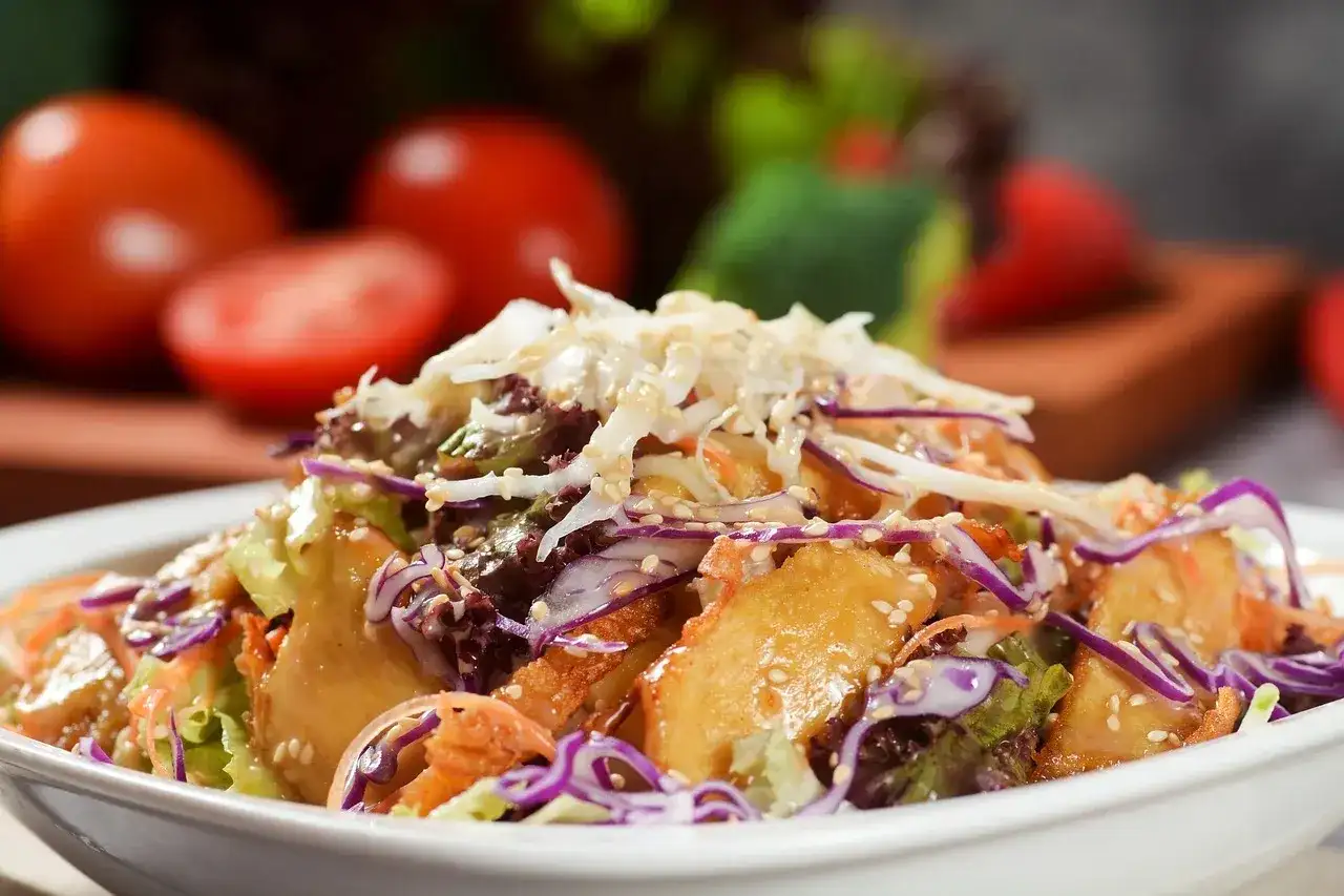 Kolorowa surówka z kapusty, marchewki i sałaty, posypana sezamem, na białym talerzu.