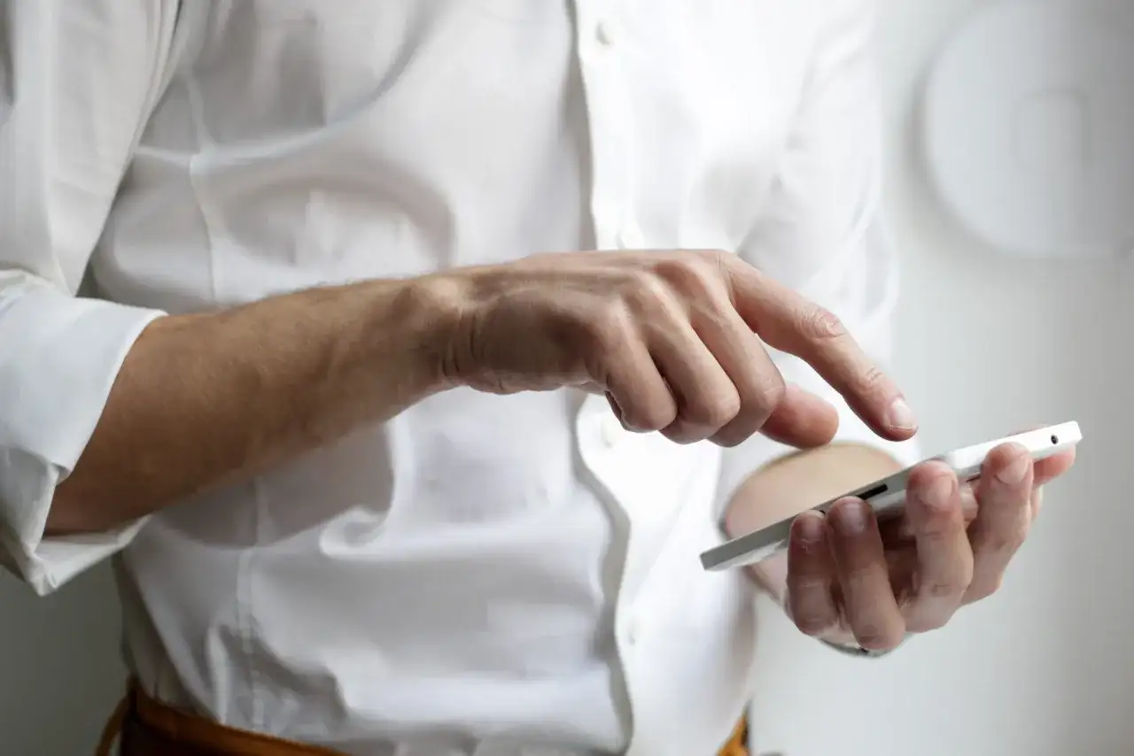 Mężczyzna w białej koszuli prowadzi rozmowę telefoniczną po angielsku, dotykając ekranu smartfona.