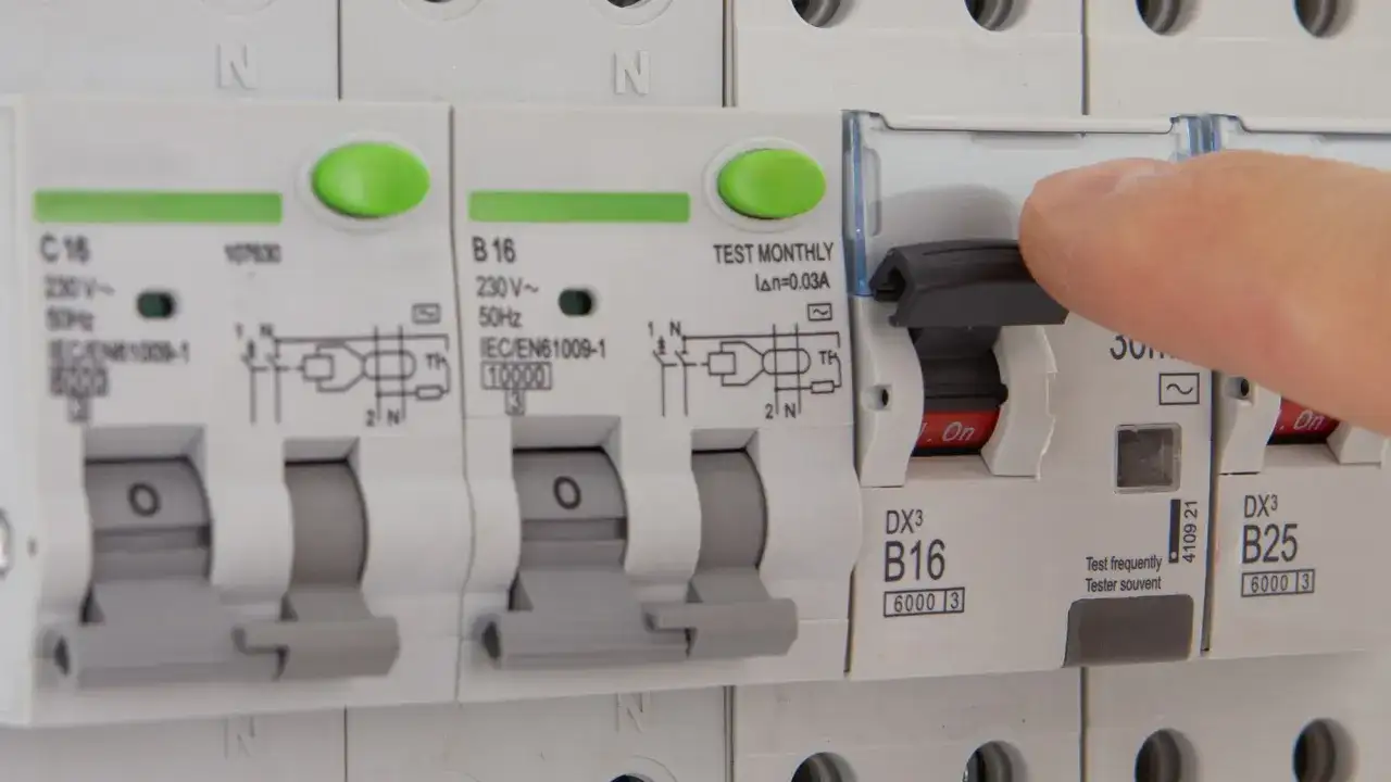 Dłoń naciska dźwignię wyłącznika, który jest częścią instalacji elektrycznej. Czy różnicówka jest obowiązkowa? To pytanie o bezpieczeństwo.