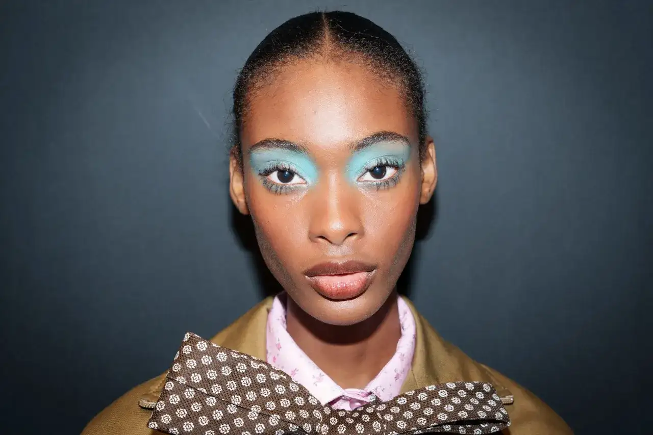 Modelka z turkusowymi cieniami do powiek i kokardą. Modne makijaże na wybiegu.