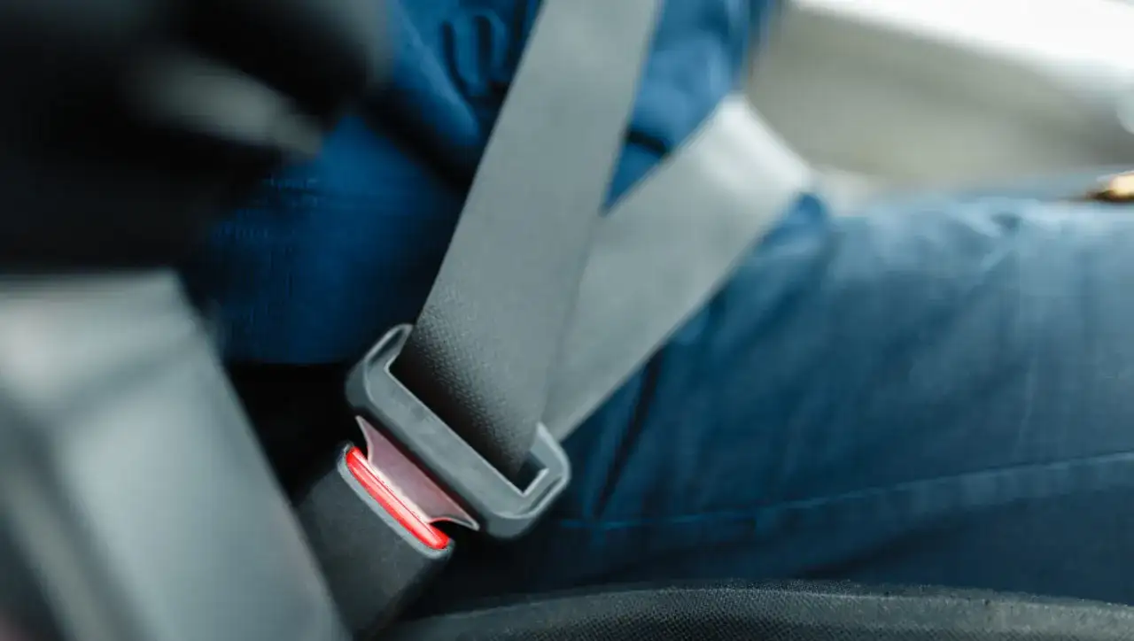 Osoba zapina środkowy pas bezpieczeństwa w samochodzie. Pasek jest wpięty w klamrę.