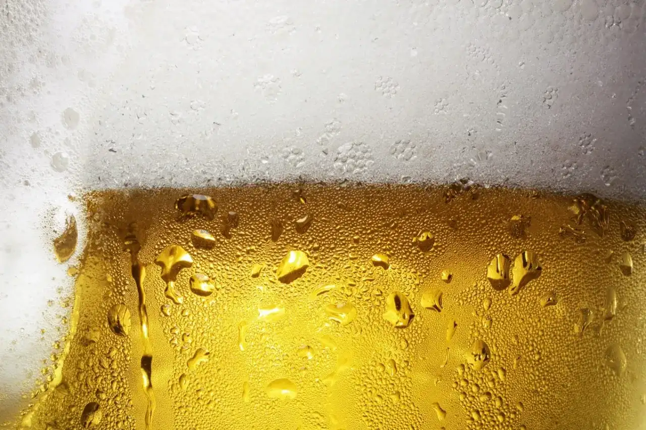 Zbliżenie na szklankę piwa z kroplami kondensacji i białą pianką na górze.