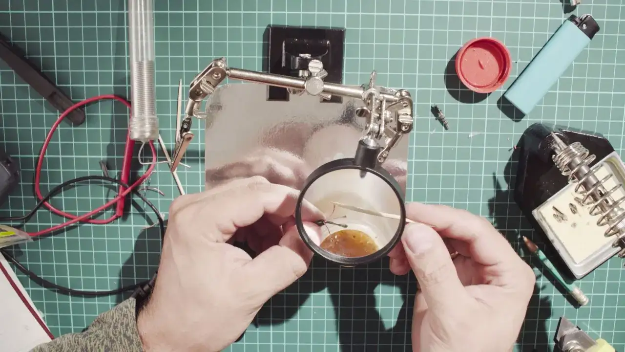 Precyzyjne lutowanie przewodów 230v pod lupą. W tle lutownica i zapalniczka.