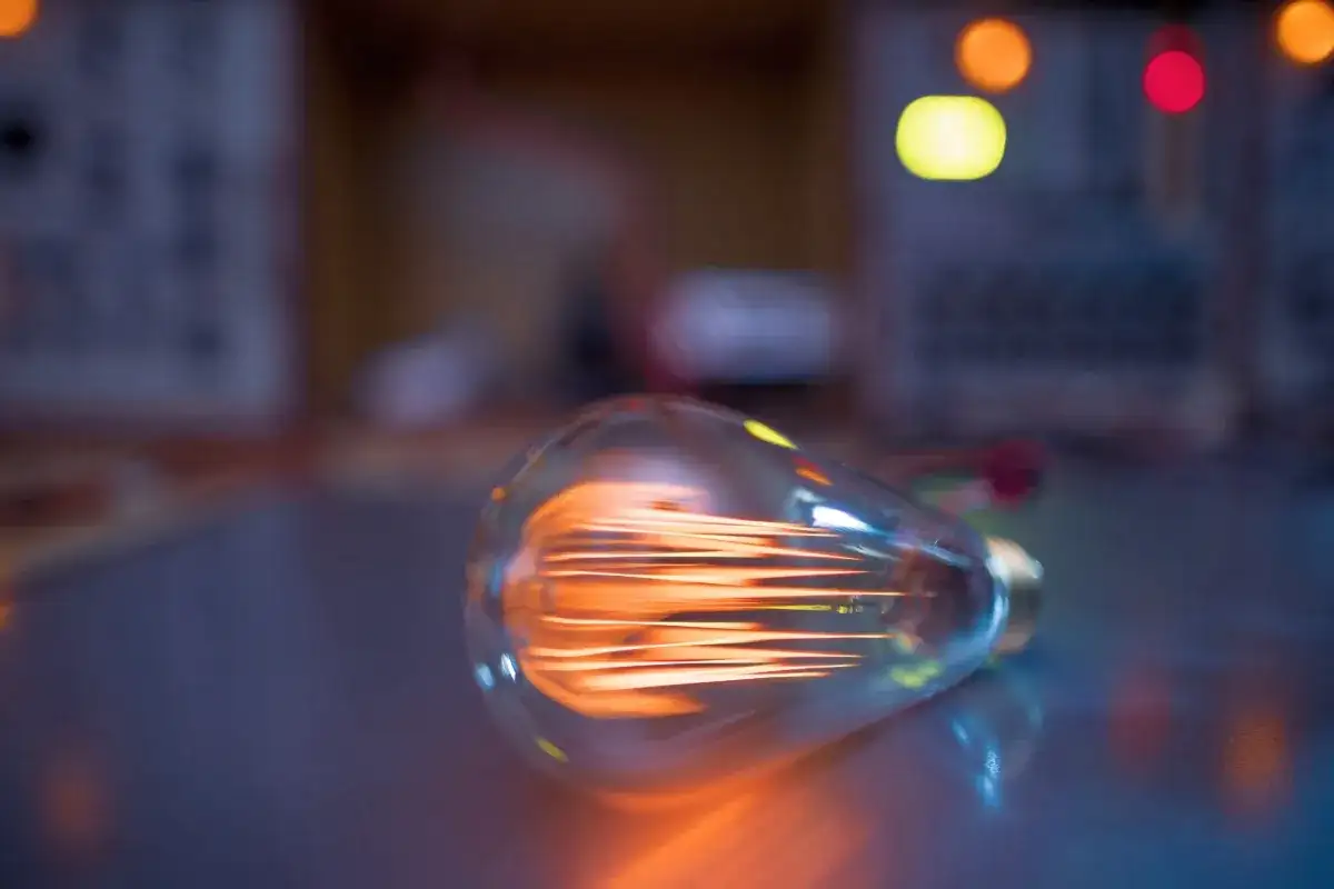 Żarówka LED 3W, ile to wat? Widoczna żarówka z rozżarzonym żarnikiem, w tle kolorowe światła.