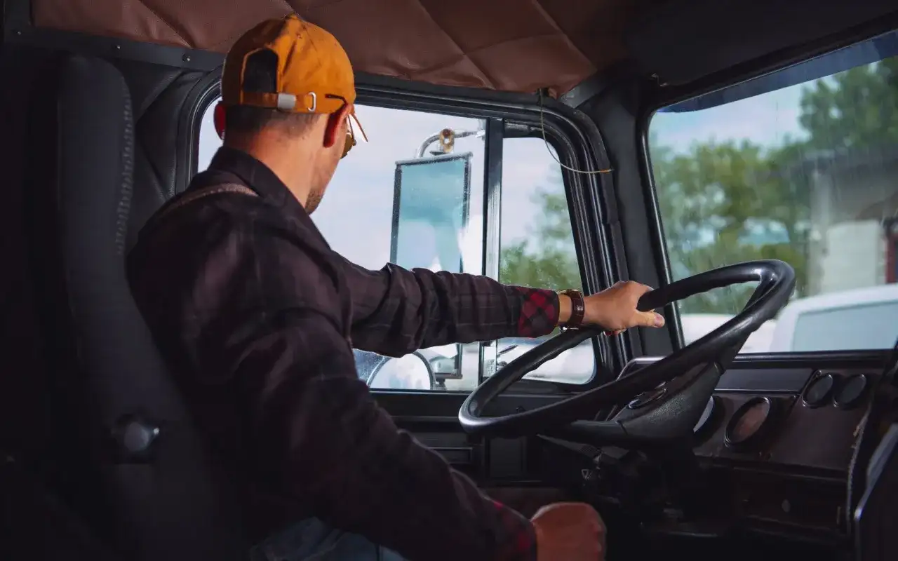 Kierowca w czapce i koszuli w kratę trzyma kierownicę. Pamiętaj o regularnym szkoleniu BHP kierowcy co ile.