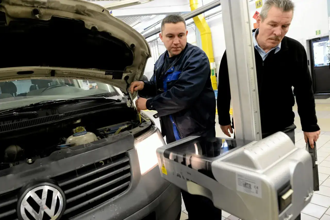 Mechanik sprawdza samochód z otwartą maską, obok stoi urządzenie do ustawiania świateł.