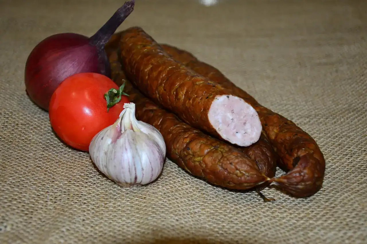 Kiełbasa, cebula, pomidor i czosnek na płóciennym tle.