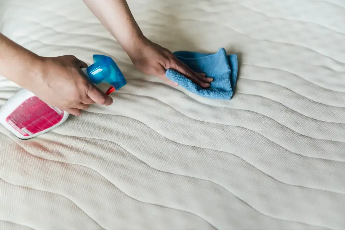 Czyszczenie materaca: ręka z butelką sprayu i ściereczką usuwa nieprzyjemny zapach z materaca.