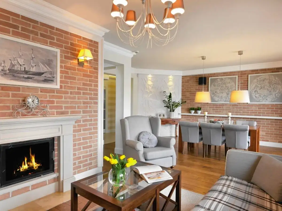 Przytulny kominek w salonie z palącym się ogniem, obok wygodny fotel i stolik kawowy.