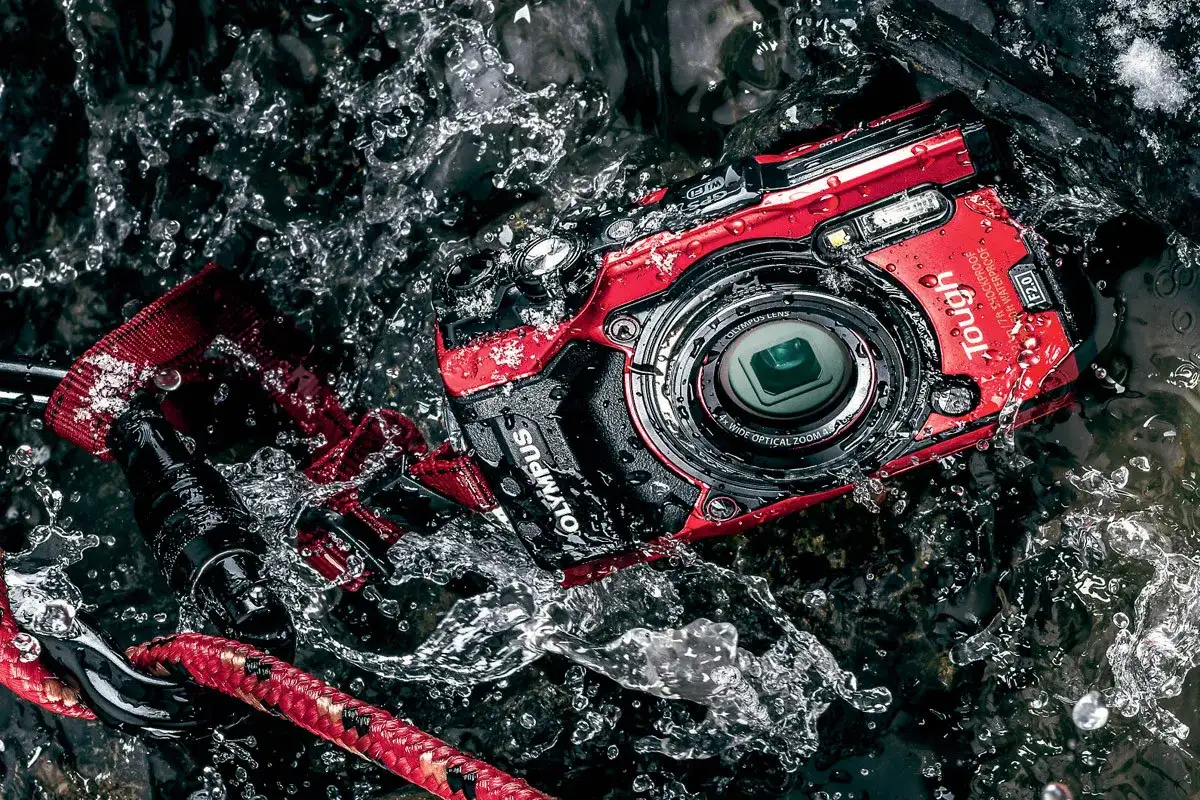 Czerwony, pancerny aparat Olympus Tough w akcji, zanurzony w wodzie. Idealny aparat do zdjęć podwodnych dla poszukiwaczy przygód.