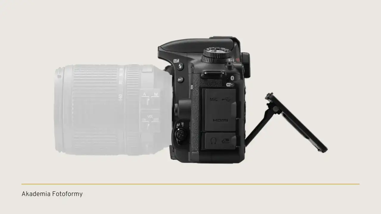 Aparat lustrzanka Nikon z obiektywem, widok z boku. Wyświetlacz uchylony, widoczne porty HDMI i mikrofonu.