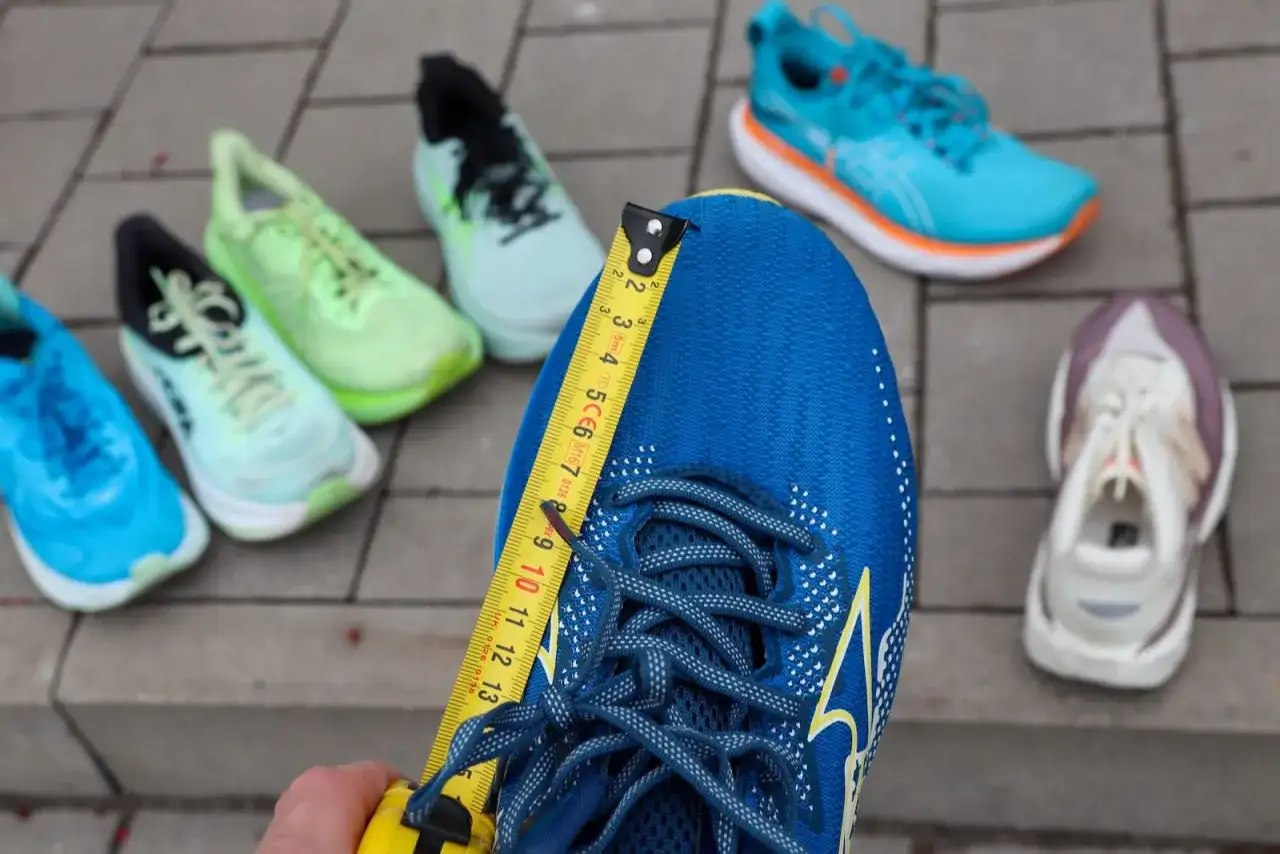 Miarka mierzy niebieskie buty do biegania. Czy buty do biegania powinny być większe? W tle inne kolorowe buty.