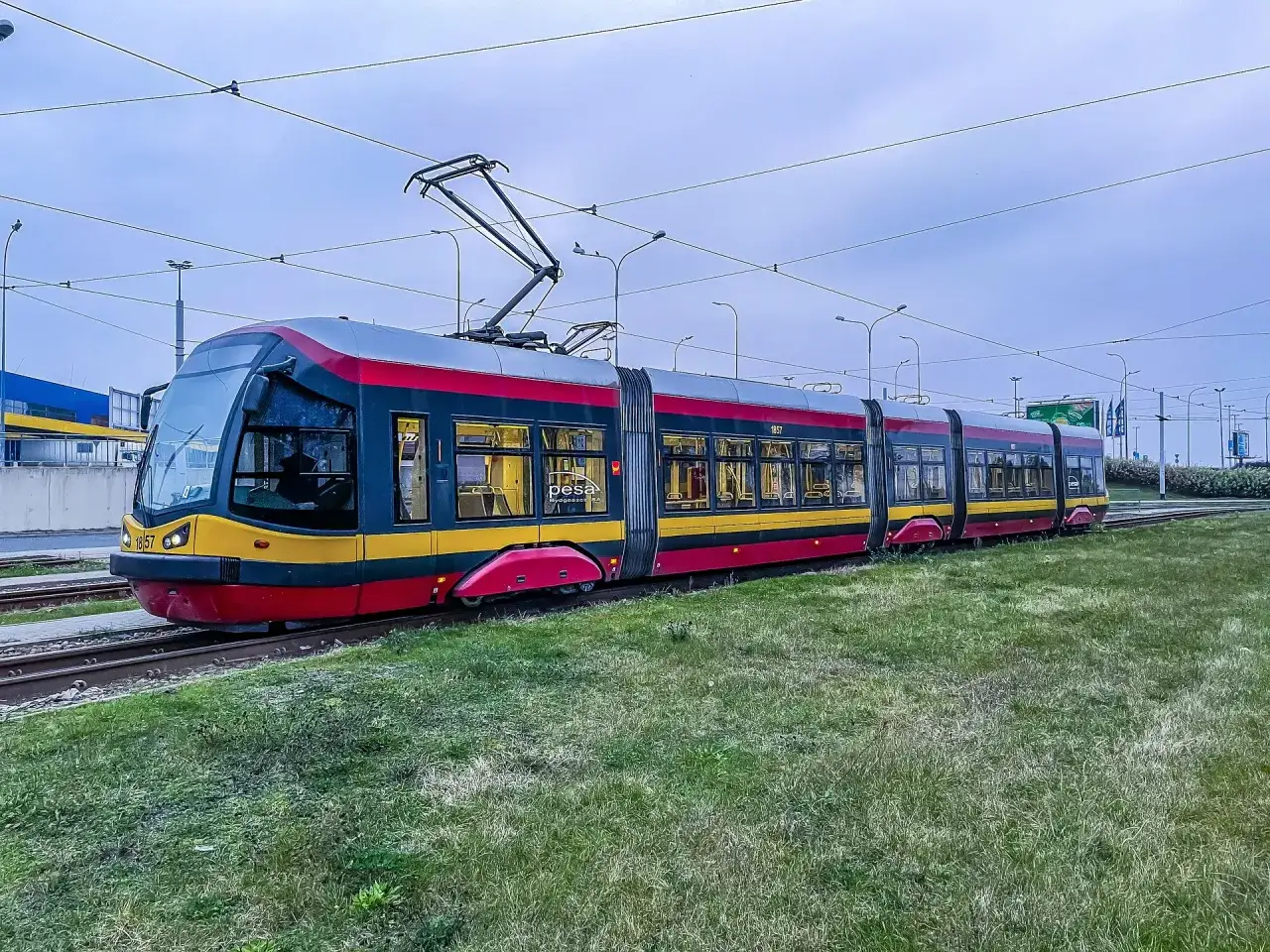 Nowoczesny tramwaj Pesa na torach, otoczony zielenią. Czy tramwaj ma zawsze pierwszeństwo? To pytanie zadaje sobie wielu kierowców.