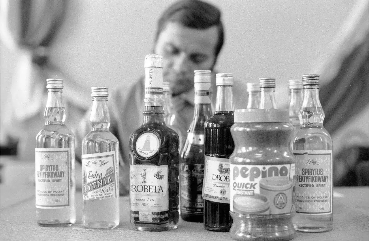 Mężczyzna bada butelki z alkoholem, w tym wódkę i brandy. Proces kupażowania może prowadzić do mętnienia wódki po dodaniu wody.