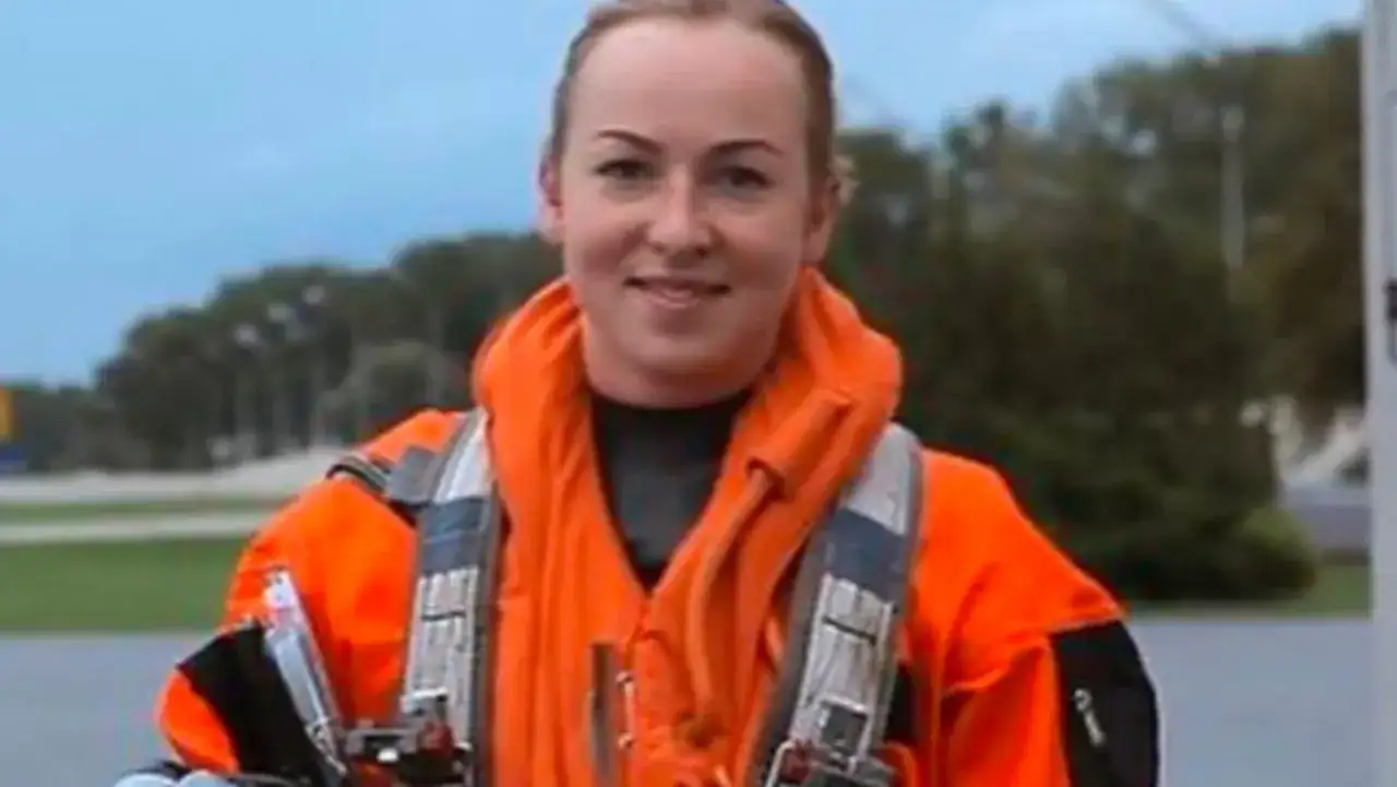 Pilotka MiG-29 w pomarańczowym kombinezonie i kamizelce ratunkowej.
