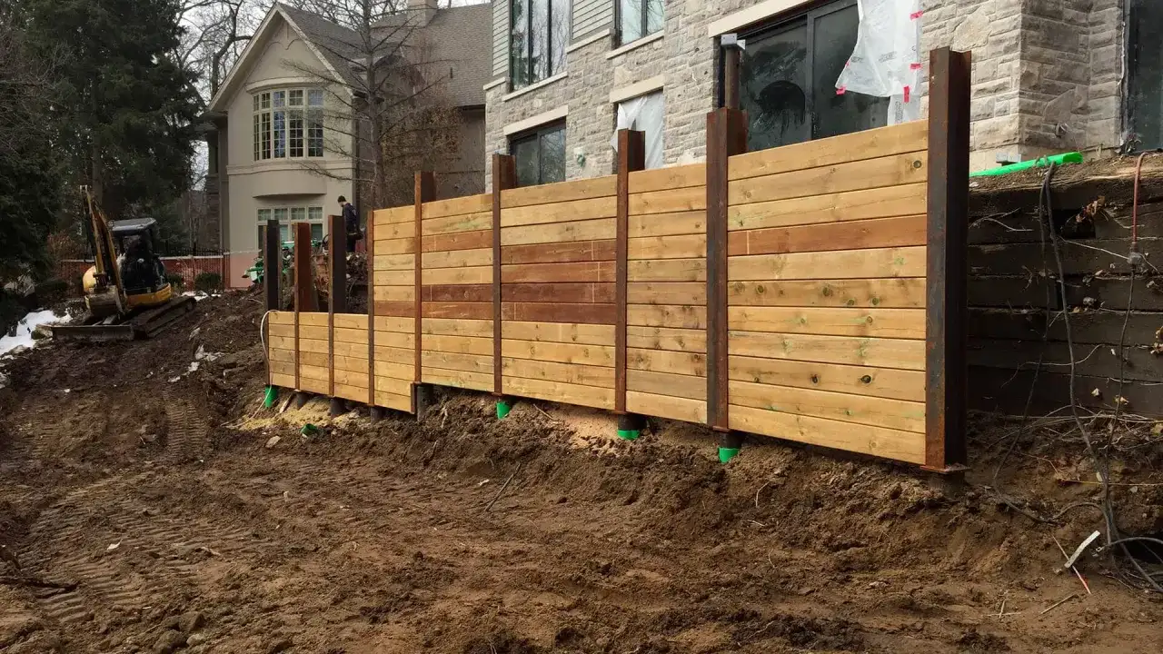 Solidny murek oporowy z drewna, budowany przy użyciu stalowych słupów, stabilizuje skarpę obok domu.