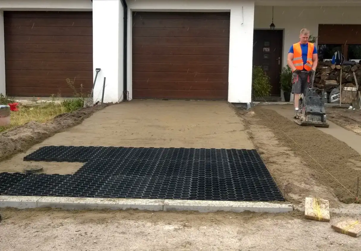 Pracownik zagęszcza podłoże pod podjazd, gdzie układana jest już jaka geokrata na podjazd.