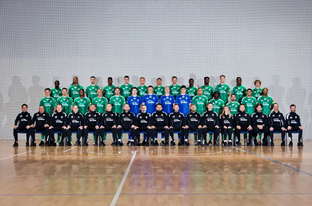 Radomiak Radom zawodnicy w zielonych strojach pozują do wspólnego zdjęcia. W tle siatka, na pierwszym planie parkiet.