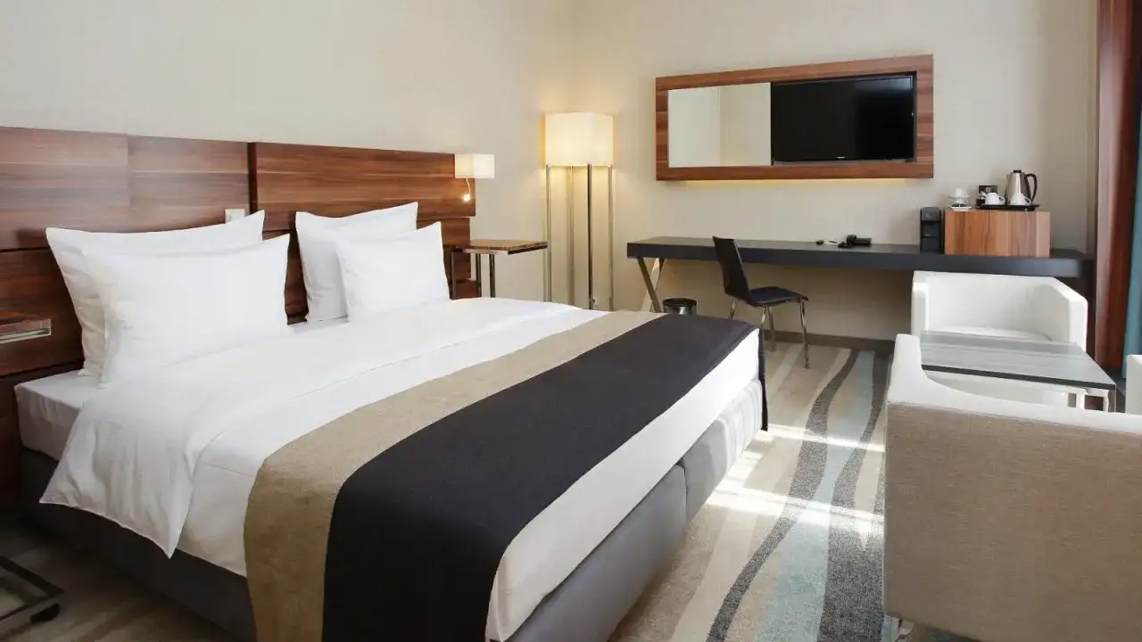 Nowoczesne wyposażenie pokoi hotelowych: wygodne łóżko, biurko z TV, fotele i stolik.