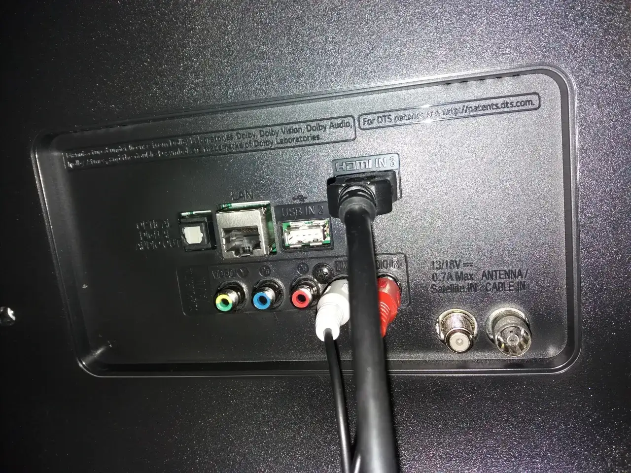 Tył telewizora z podłączonymi kablami HDMI, USB, LAN i audio.