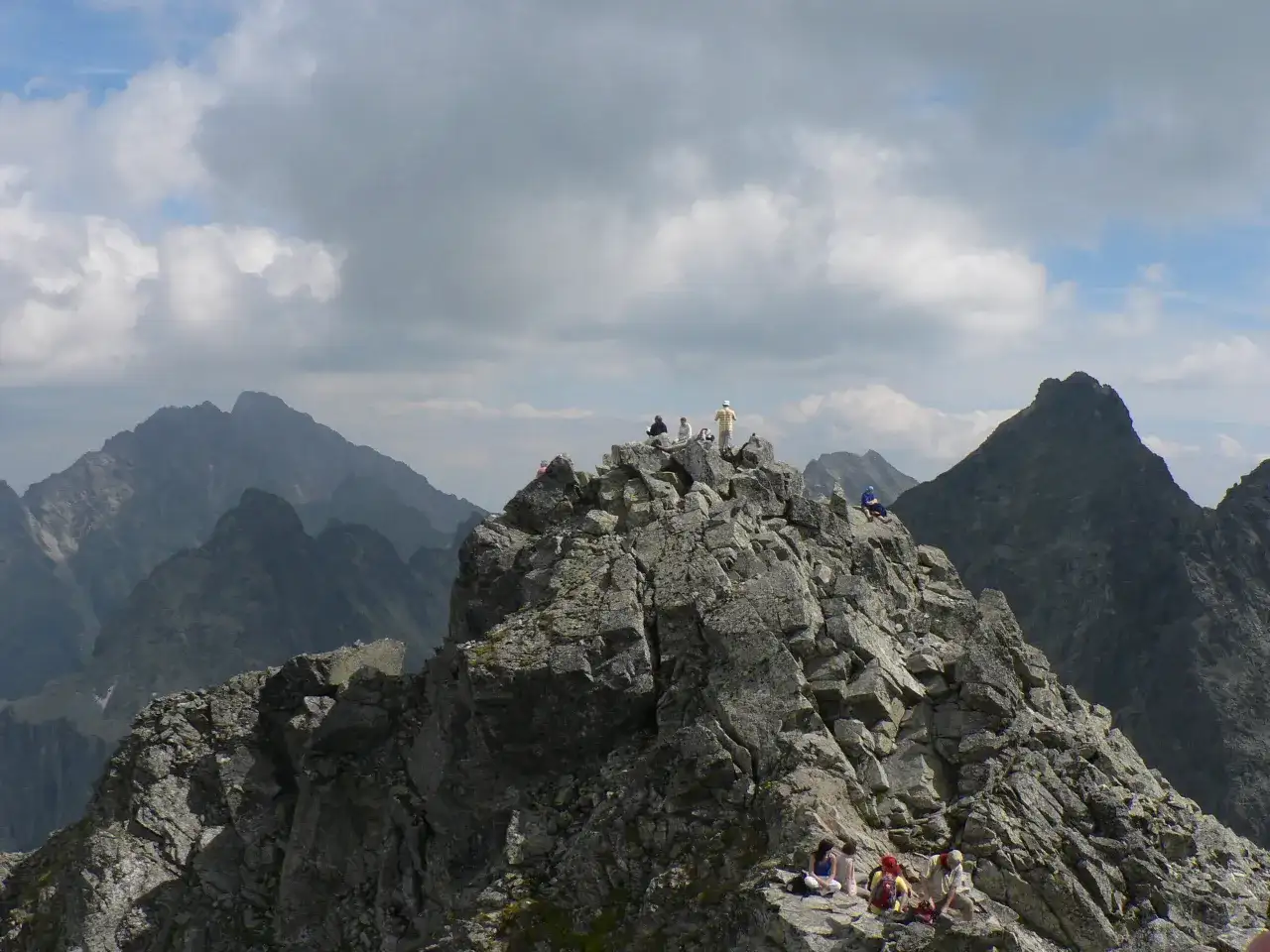 Grupa turystów odpoczywa na skalistym szczycie, podziwiając widok na Tatry. Trasa na Rysy jest wymagająca, ale widoki wynagradzają wysiłek.