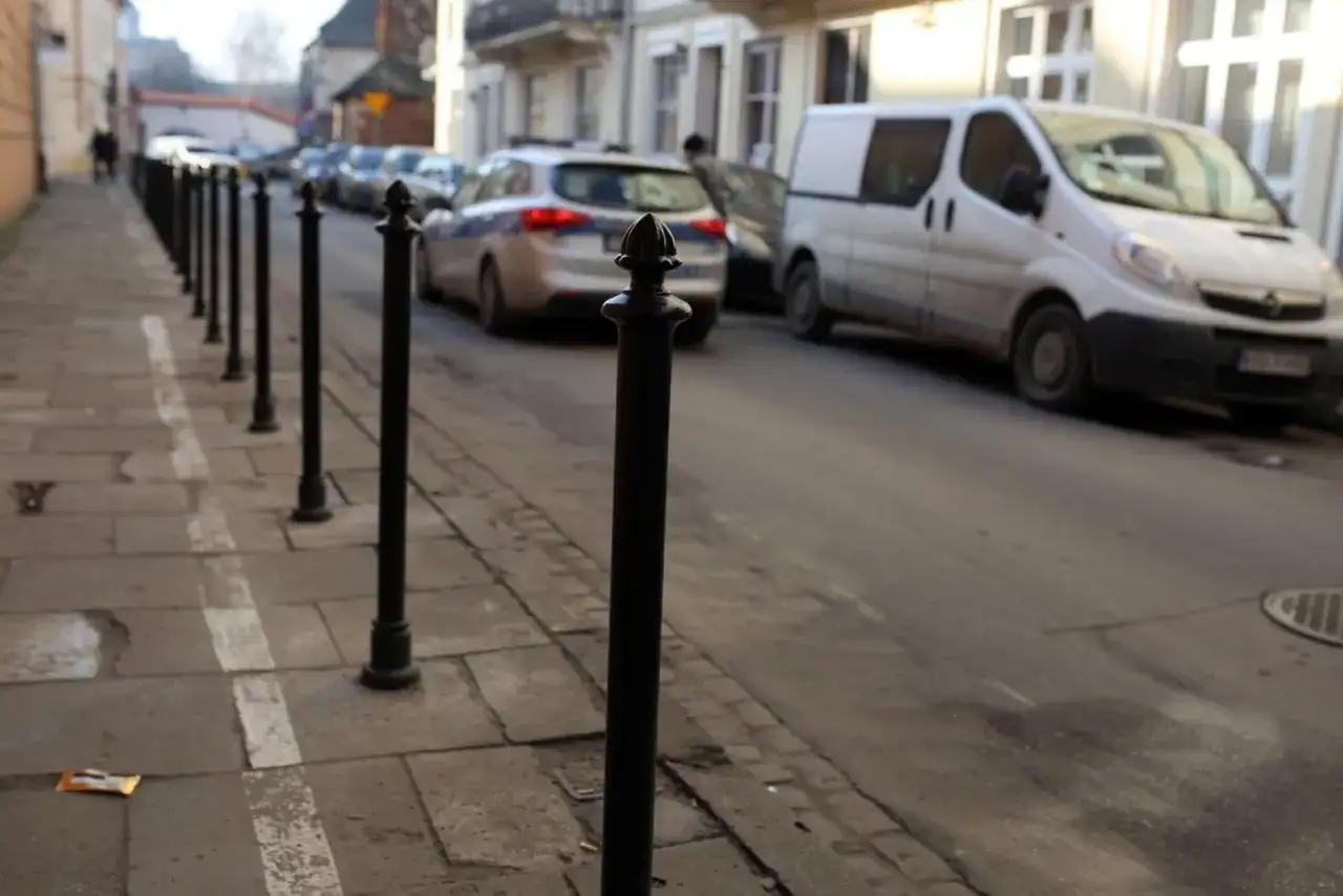 Słupek chodnikowy, radiowóz i biały van na ulicy.