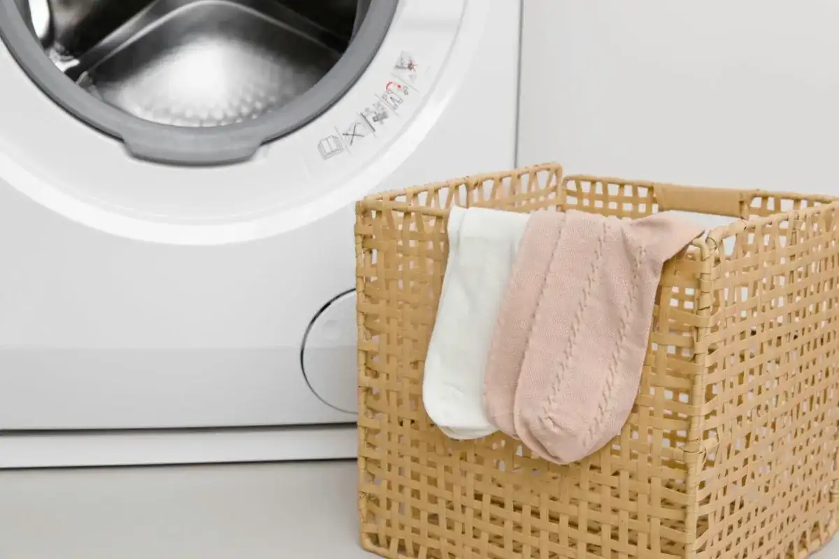 Biała pralka i wiklinowy koszyk z dwoma parami skarpetek: białą i różową.
