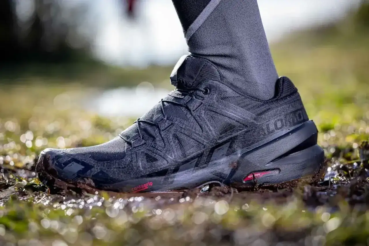 Czarny but Salomon z technologią Contagrip, pewnie stąpający po błotnistym, mokrym terenie.
