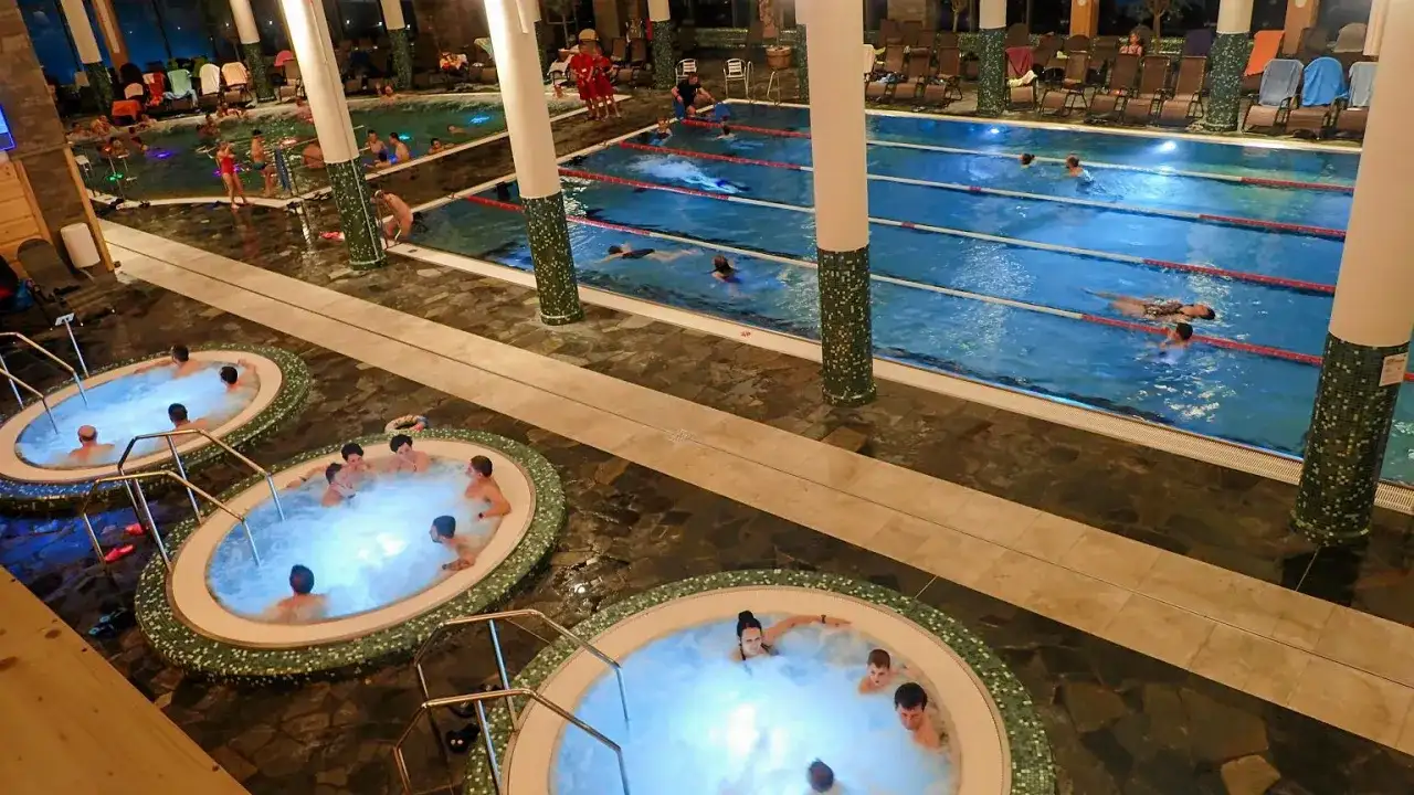 Widok na baseny termalne z jacuzzi i pływającymi ludźmi.