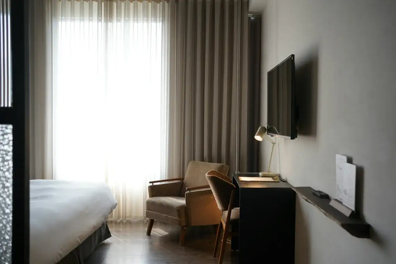 Przytulny pokój hotelowy z wygodnym łóżkiem, fotelem i biurkiem. Zastanawiasz się, ile kosztuje nocleg w takim miejscu?