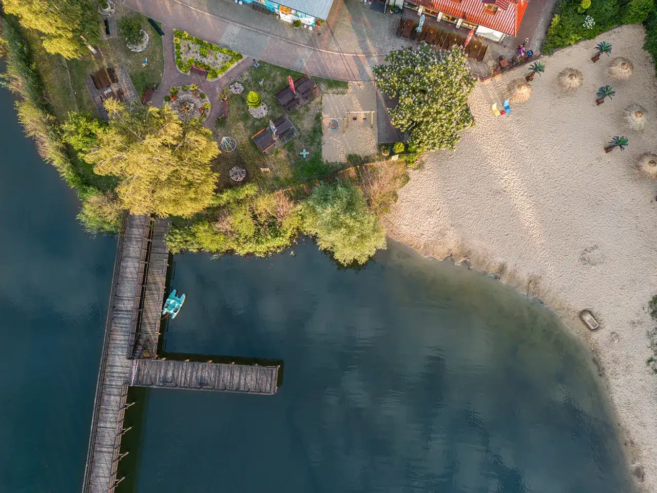 Widok z lotu ptaka na drewniane molo, plażę i jezioro z łódką.