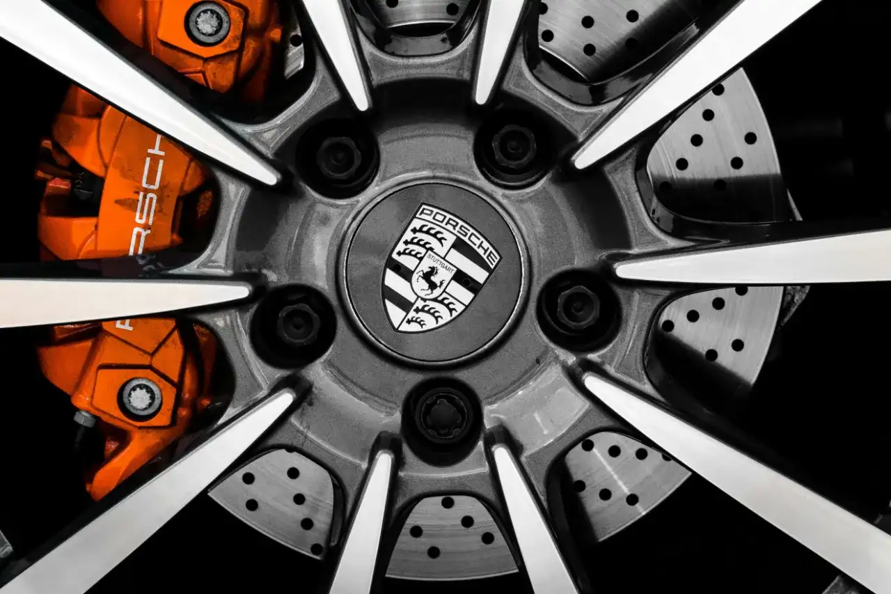 Zbliżenie na felgę Porsche z pomarańczowymi zaciskami hamulcowymi i logo marki.