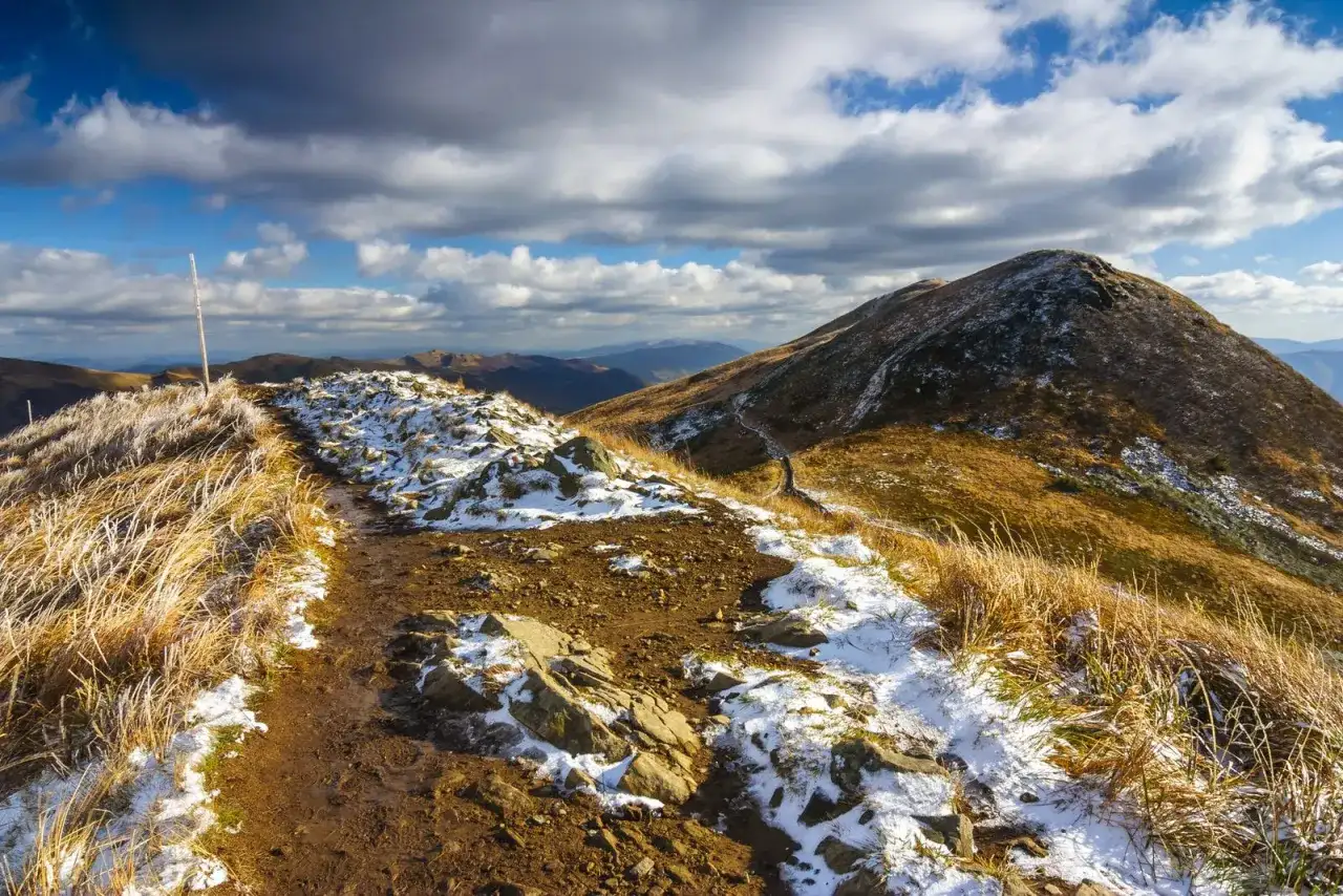 Szlak przez Bieszczady na Ukrainę, pokryty pierwszym śniegiem i jesienną trawą, pod burzowym niebem.