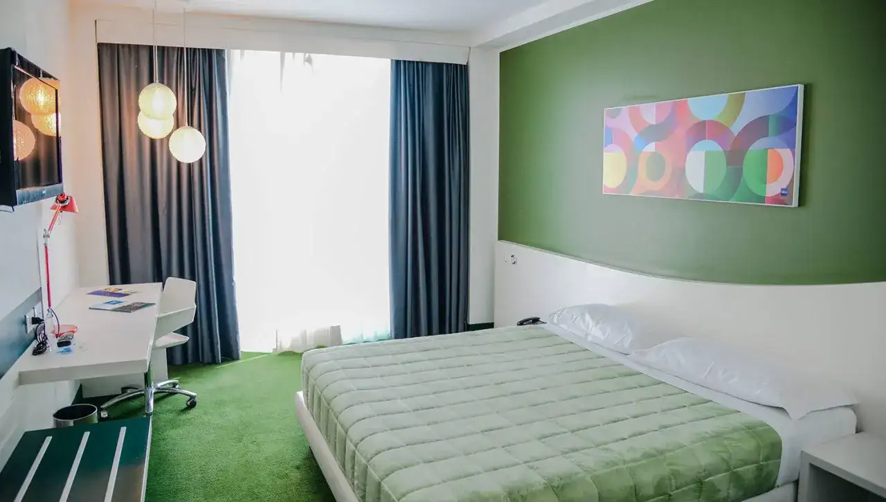 A modern hotel room with a green bedspread, green carpet, and a colorful abstract art piece on a green wall.