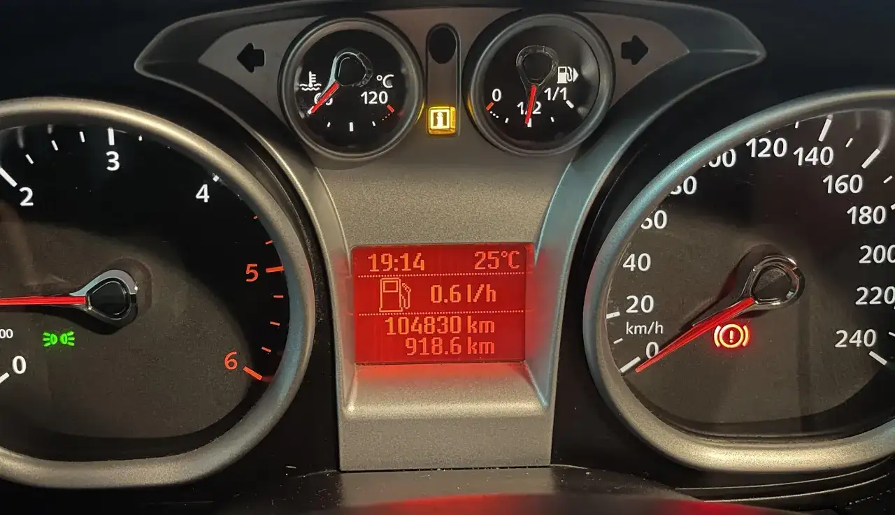 Deska rozdzielcza Ford Focus z kontrolkami: temperatura, paliwo, przebieg, prędkościomierz i kontrolka hamulca ręcznego.