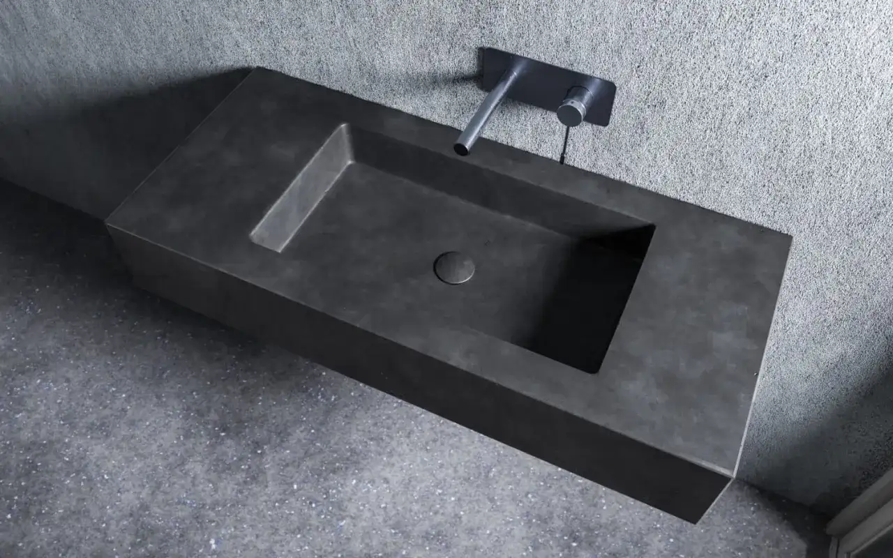 Nowoczesna umywalka z betonu o minimalistycznym designie, z wpuszczonym w blat odpływem i elegancką baterią ścienną.