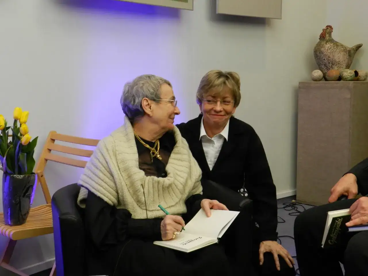 Dwie kobiety rozmawiają, jedna pisze w notatniku, by ocalić od zapomnienia wiersz.