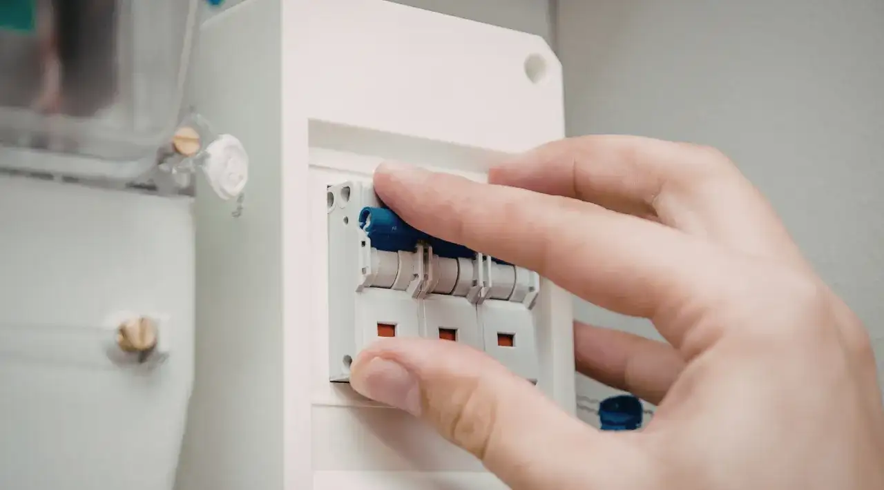 Dłoń manipuluje wyłącznikami w skrzynce elektrycznej. Dowiedz się, jak dobrać zabezpieczenie prądowe.