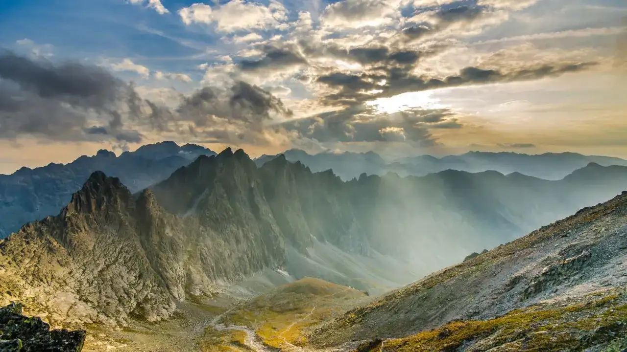 Słoneczne promienie przebijają się przez chmury nad skalistą przełęczą w Tatrach. Widok zapiera dech w piersiach.