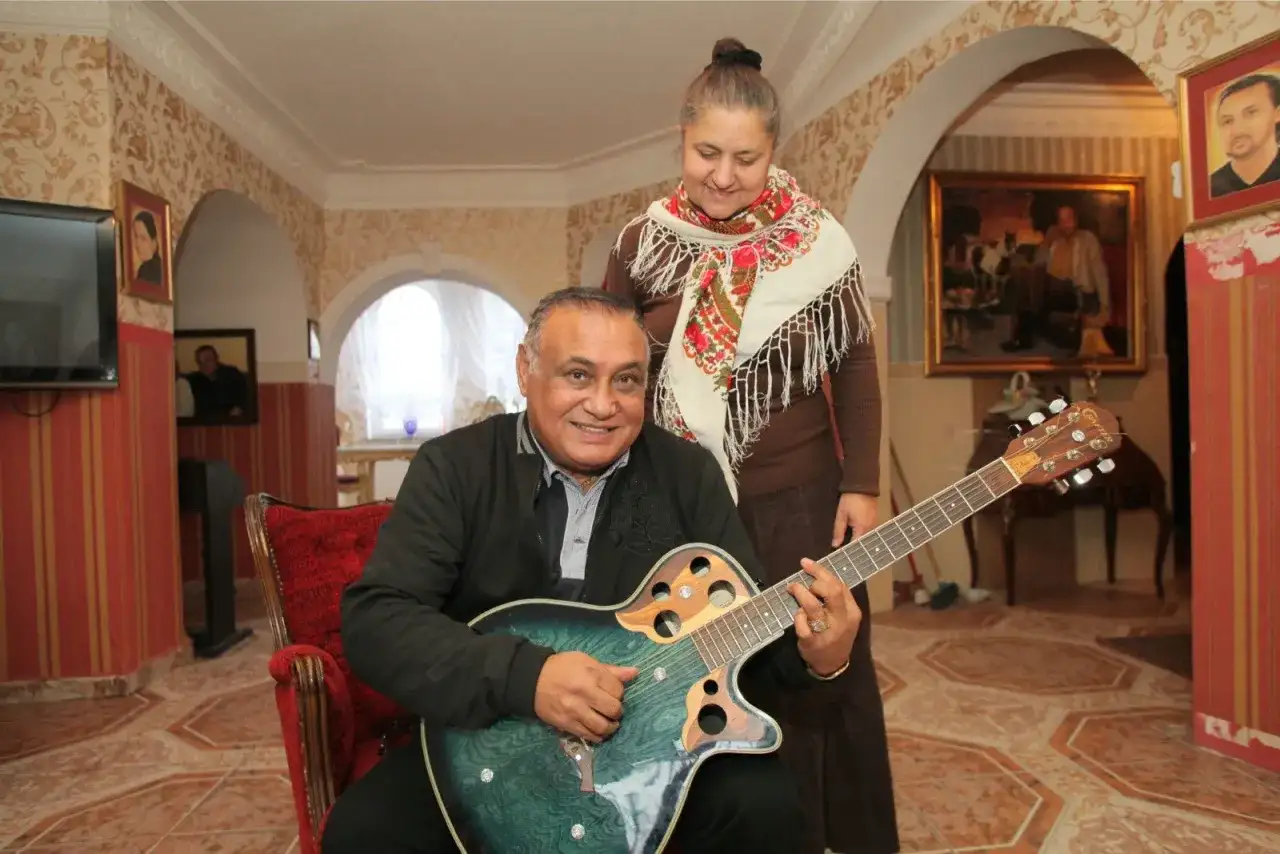 Uśmiechnięty mężczyzna gra na gitarze, a za nim stoi kobieta. Nie wiadomo, ile lat ma Don Vasyl, ale wygląda na szczęśliwego.
