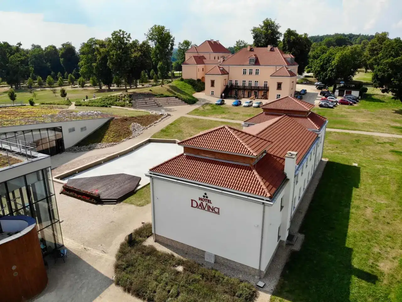 Widok z lotu ptaka na Hotel Da Vinci z czerwonym dachem, otoczony zielenią i innymi budynkami.