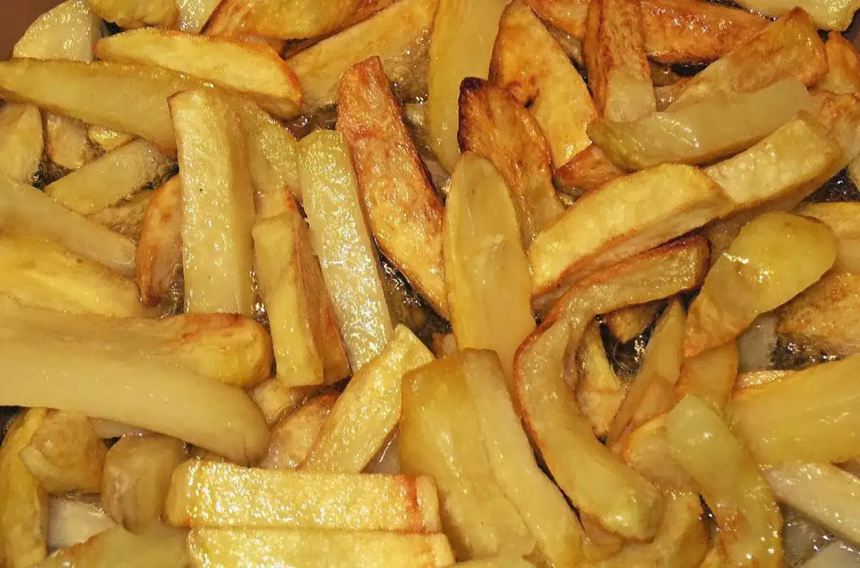 Złociste frytki smażące się na głębokim oleju na patelni.