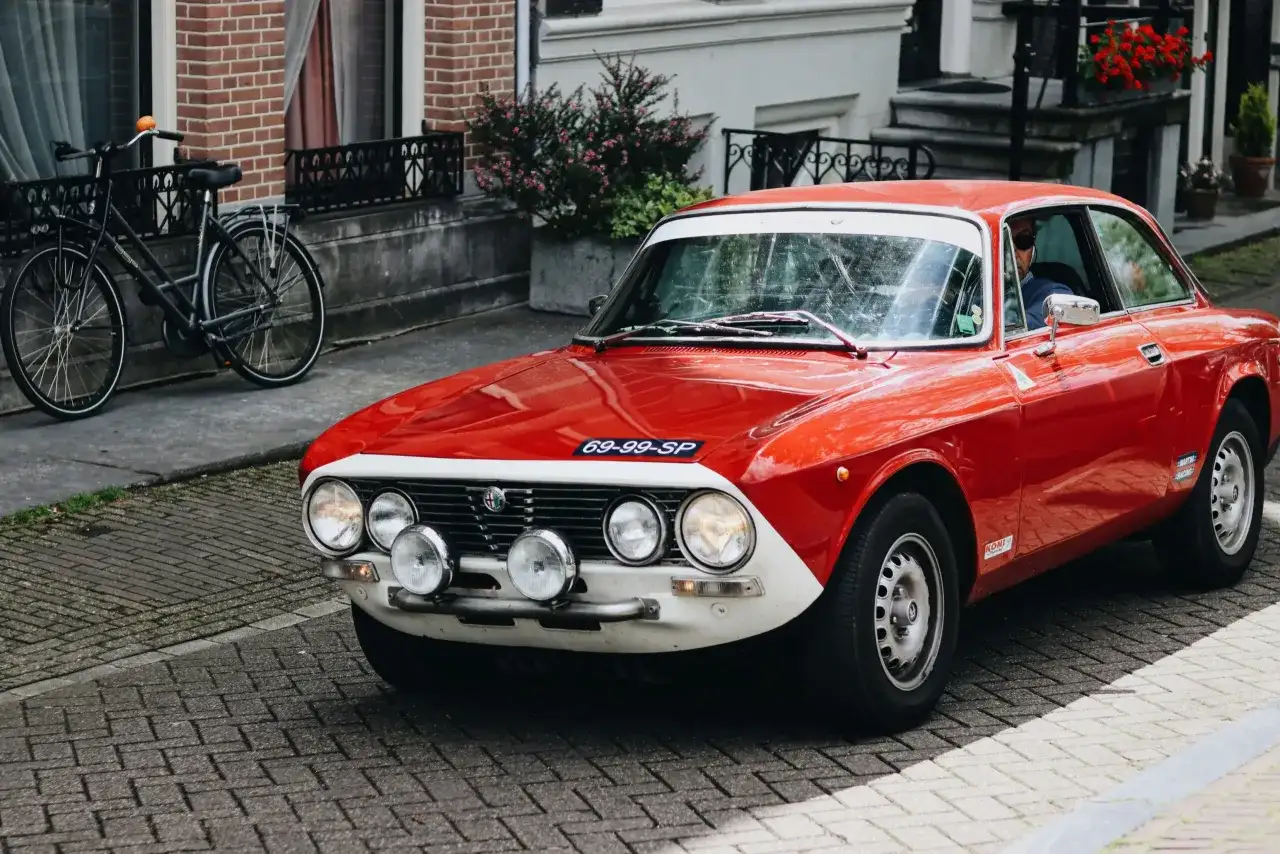 Czerwone auto sportowe Alfa Romeo z lat 70. na brukowanej ulicy, obok rower.