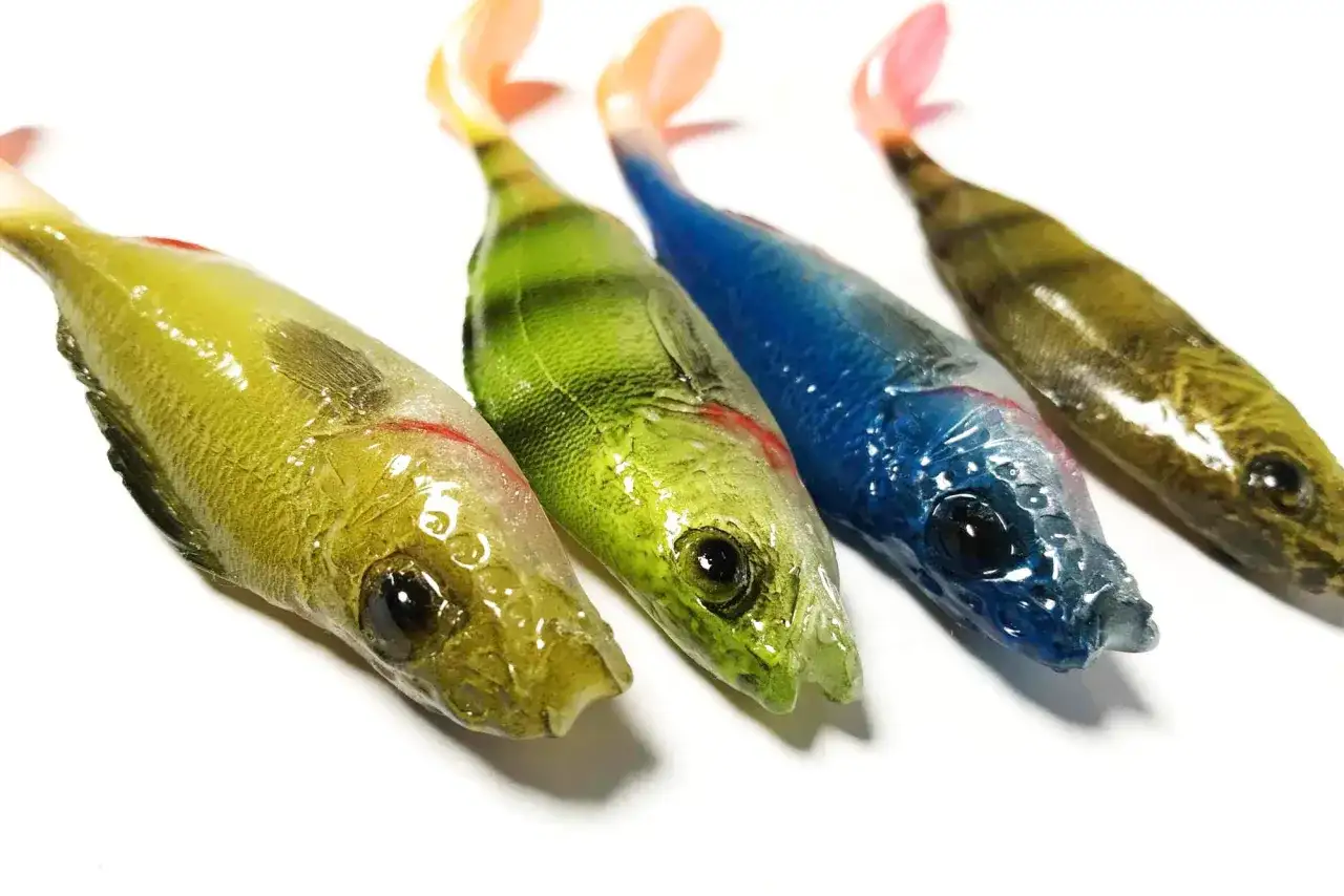 Cztery gumowe przynęty wędkarskie w kształcie rybek w różnych kolorach.