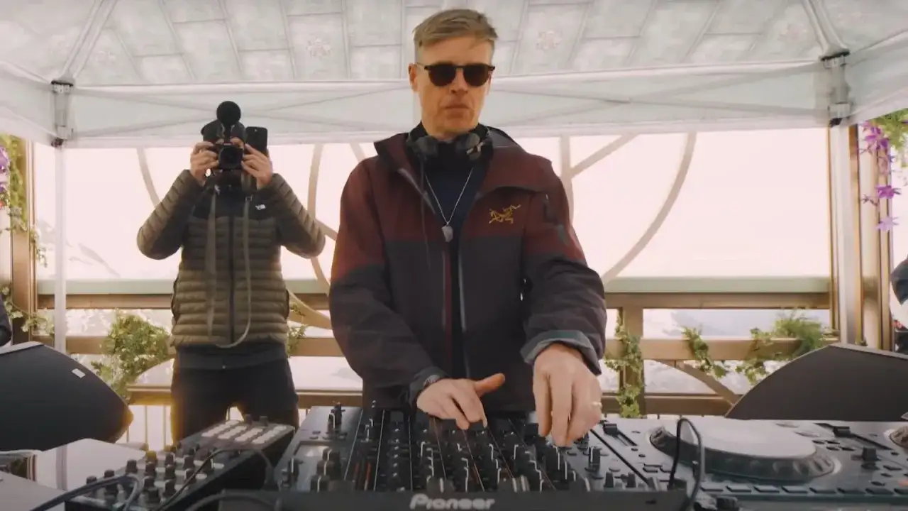 DJ w okularach i słuchawkach miksuje muzykę, a za nim operator kamery filmuje. To scena, jakiej można by się spodziewać po **najlepsi dj wszechczasów**.