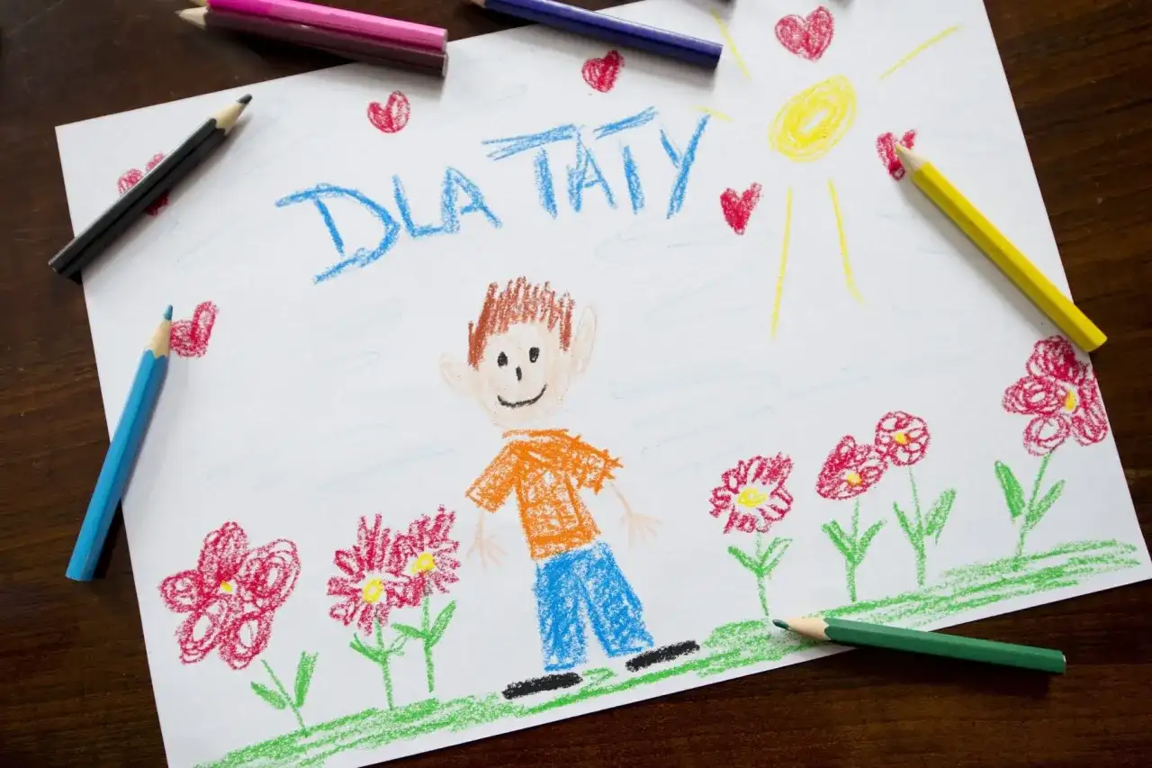 Dziecko narysowało laurkę dla taty z uśmiechniętą buzią, słońcem i kwiatami.