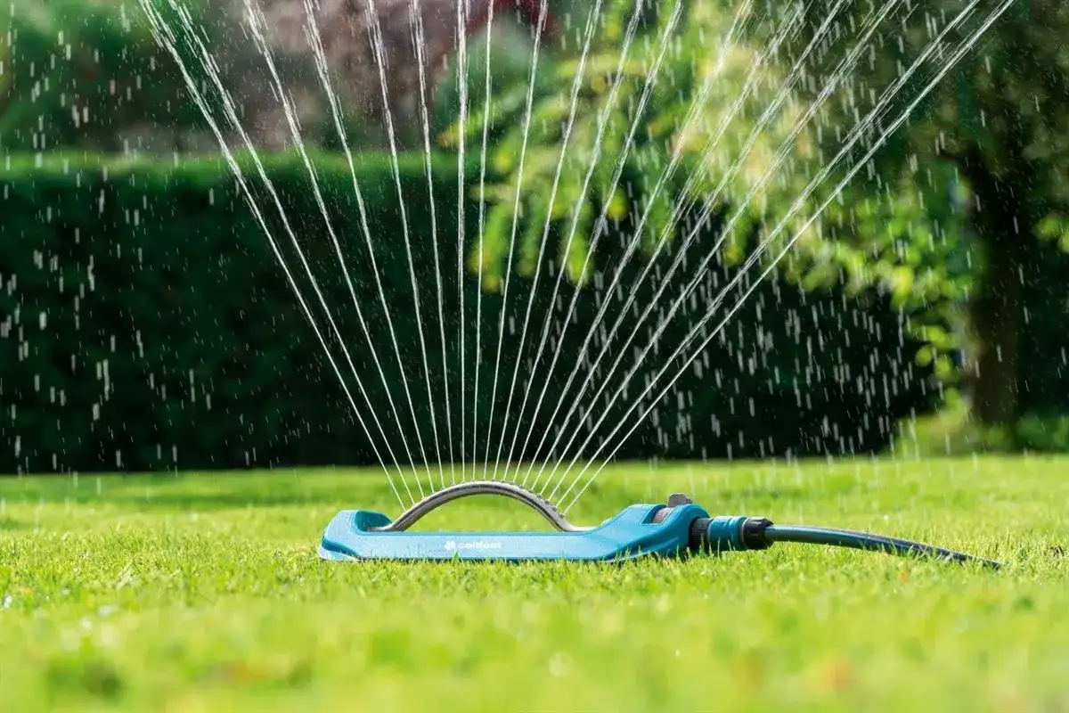 Niebieski zraszacz zrasza trawnik, tworząc wachlarz strumieni wody.