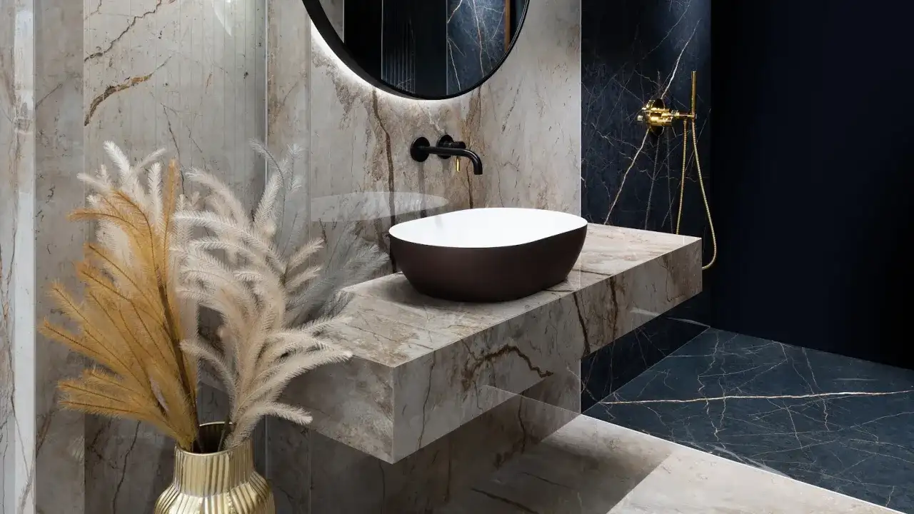 Elegancki blat pod umywalkę z płytek imitujących marmur, z umieszczoną na nim owalną umywalką i złotą armaturą.