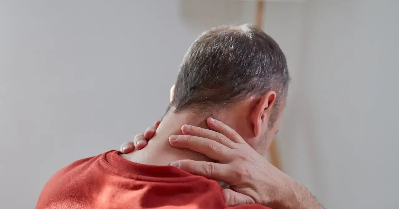 Mężczyzna masuje kark, szukając ulgi w bólu. Rozważa wdowi garb ćwiczenia w domu, by poprawić postawę.